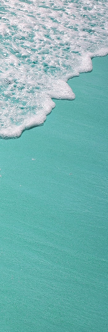Turquoise water with waves on a sandy shore.