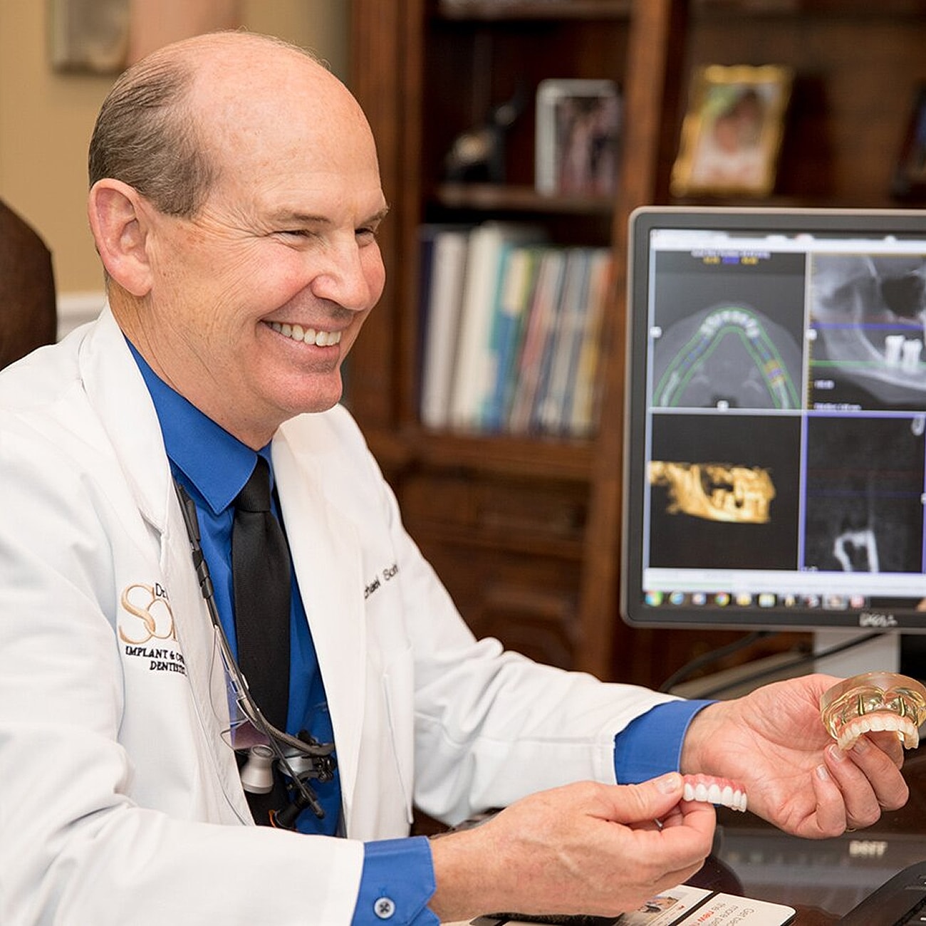 Dentist smiling with dental models and technology.