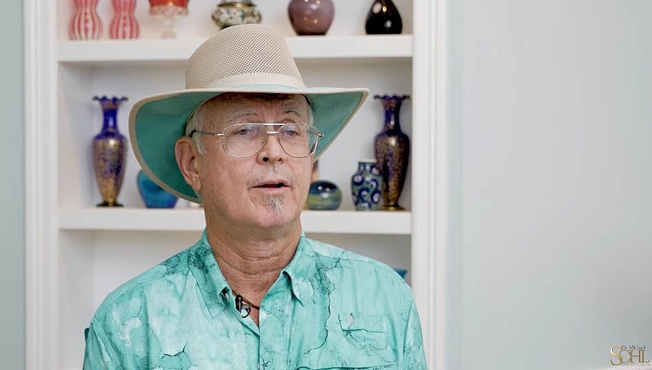 Man in a cowboy hat smiling warmly indoors.